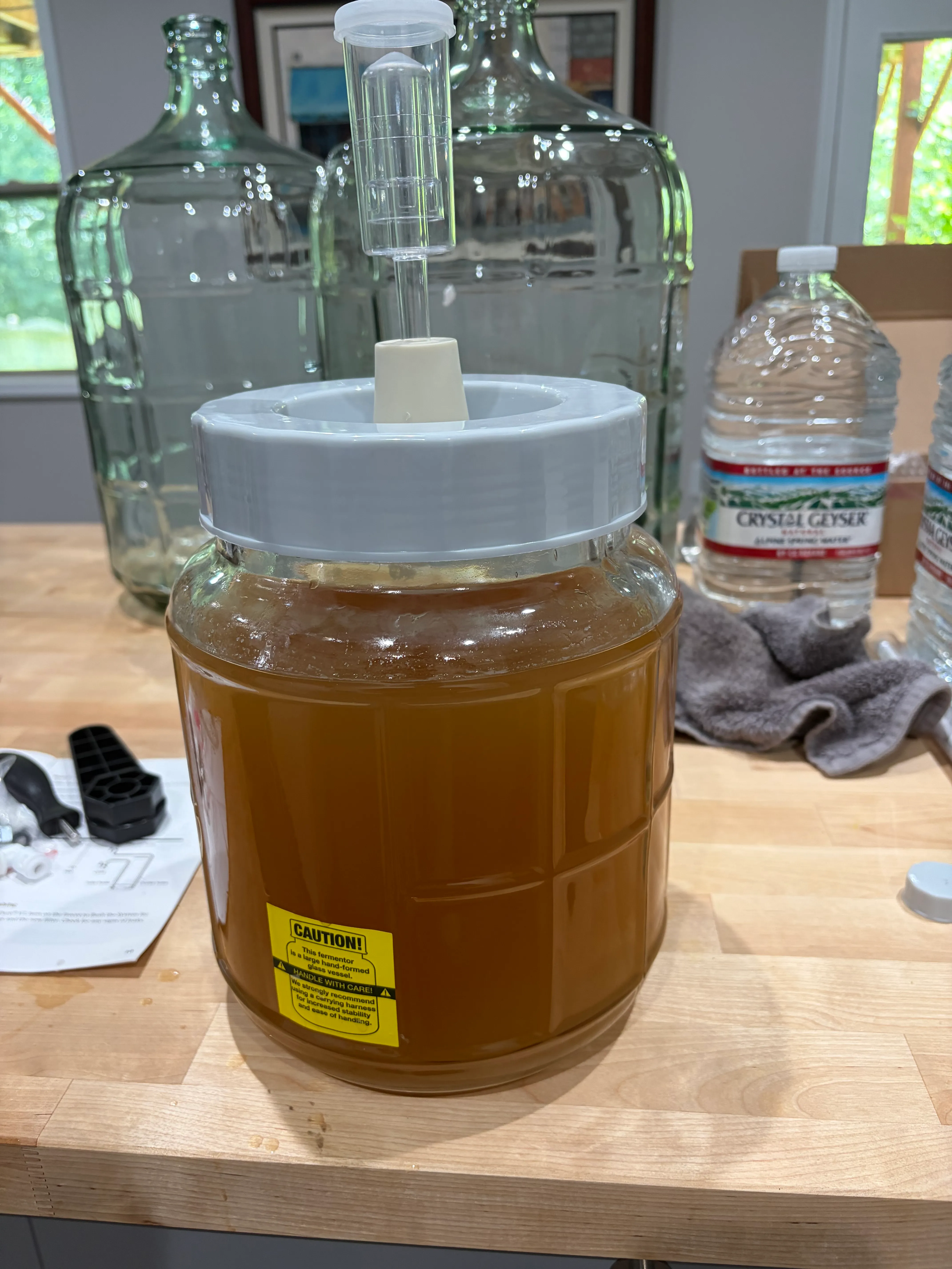Batch 1 assembled: wide-mouth gallon jar, airlock on, big carboys watching from the bench like it's their kid's first game