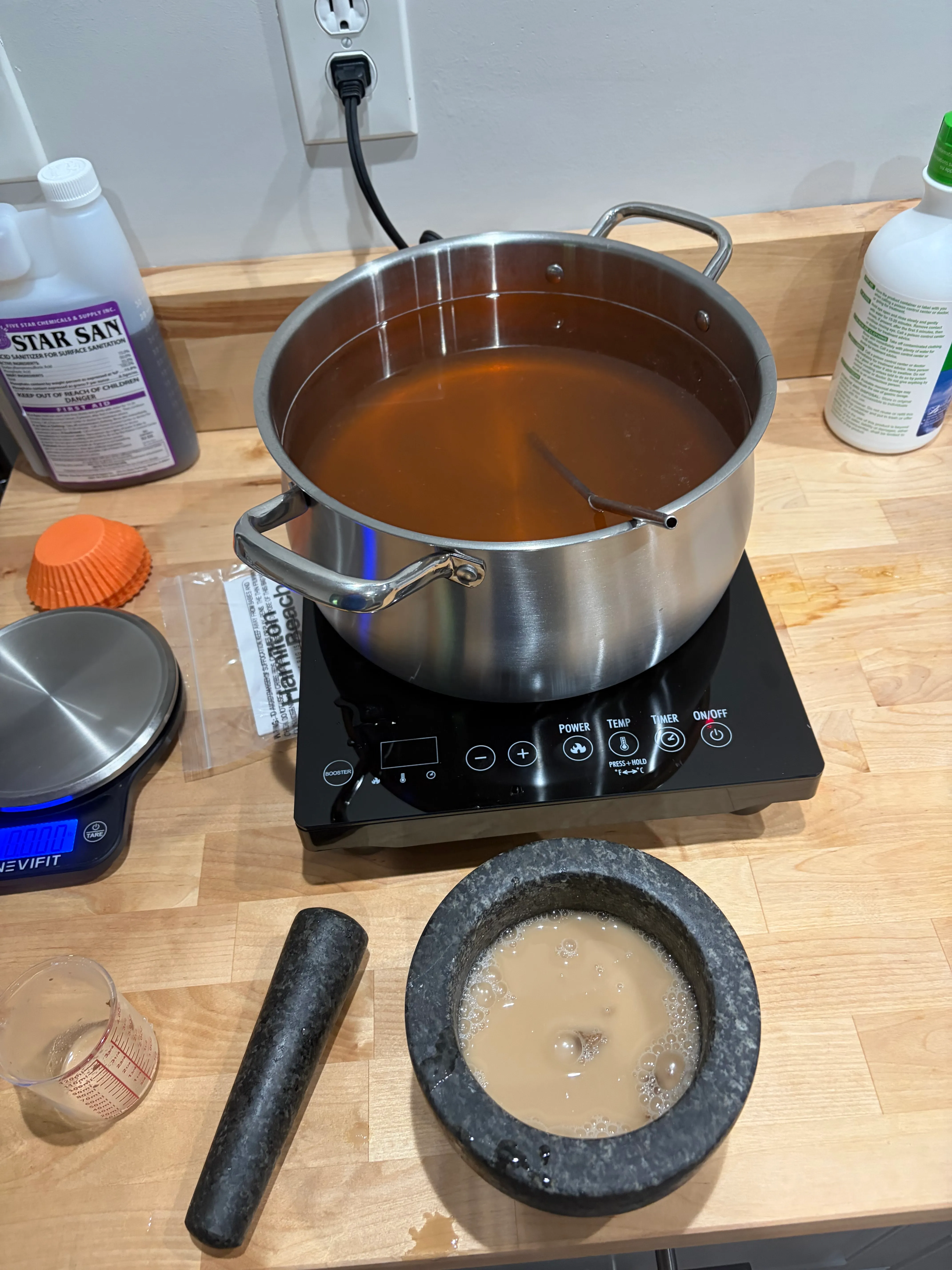 Tupelo must in the pot, dissolving on the induction burner. The molcajete out front is doing beaker duty for the yeast.