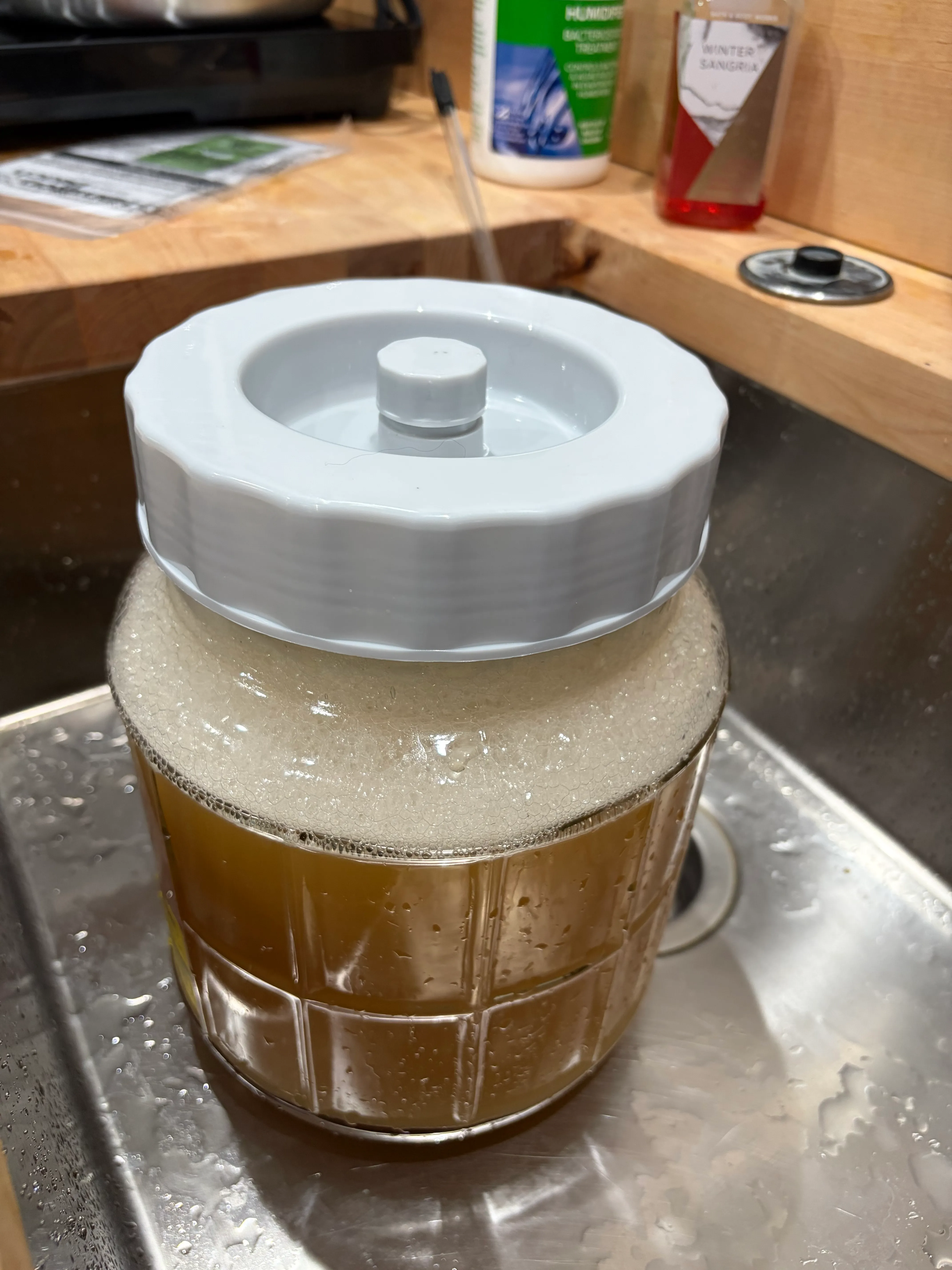 A thick foam cap of krausen on top of golden mead must in a wide-mouth fermenter.